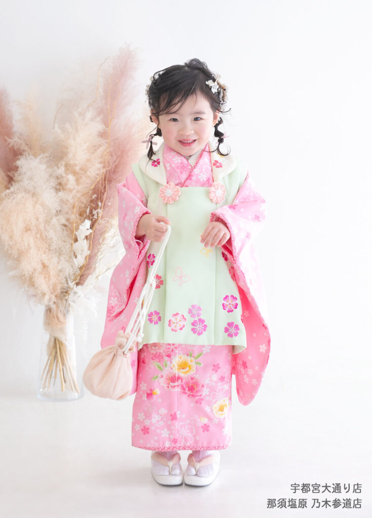 七五三3歳着物：明るいピンクに薄いグリーンの被布の着物を着た3歳の女の子。