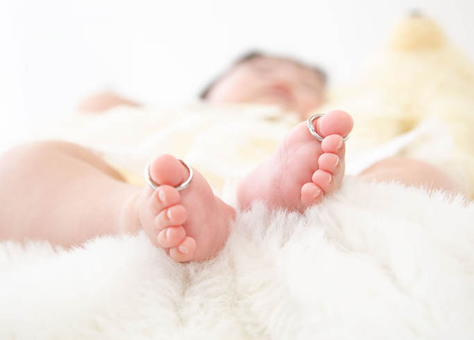 お宮参り：パパとママの結婚指輪を赤ちゃんの足の親指にかけた、小さな足がかわいらしい写真