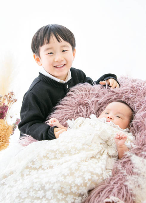 お宮参り：白いベビードレスを着た赤ちゃんとお兄ちゃんが手をつないだきょうだい写真