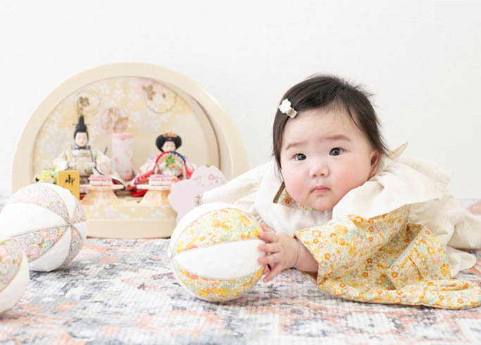 桃の節句：黄色の花柄の着物を着たひな人形と一緒の女の子の赤ちゃん。