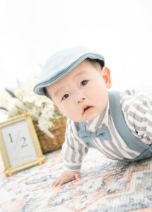 ベビーバースデー：蝶ネクタイにシャツ風のロンパースにハンチングを合わせたハイハイ姿の赤ちゃん