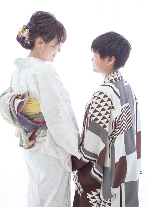 ハーフ成人：袴を着た10歳の男の子と、訪問着を着たママが手をつないで微笑み合う様子