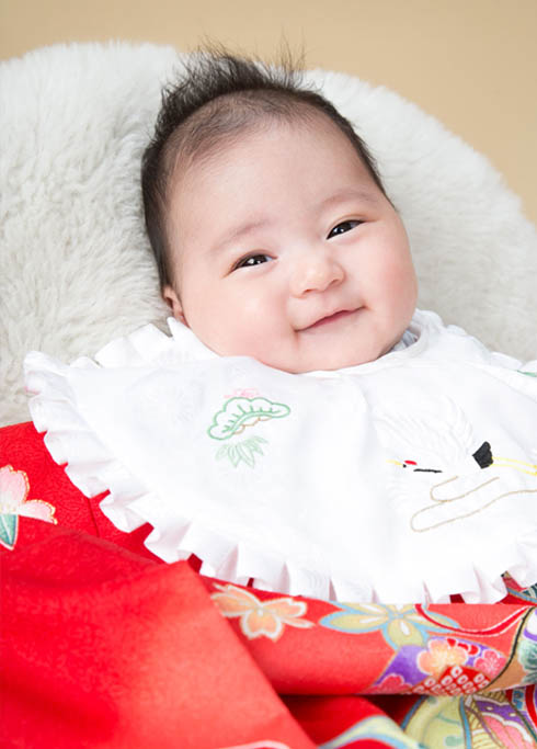 お宮参り：古典柄の赤い産着を着てにこっと笑う女の子の赤ちゃん