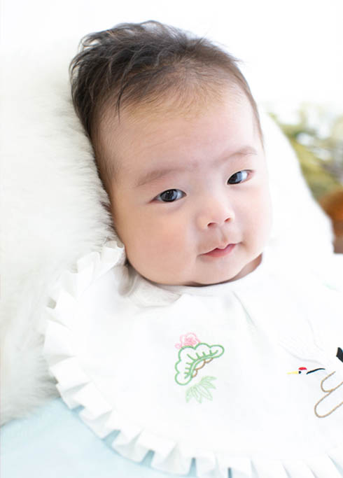 お宮参り：水色の産着を着て笑顔でこちらを見る男の子の赤ちゃん