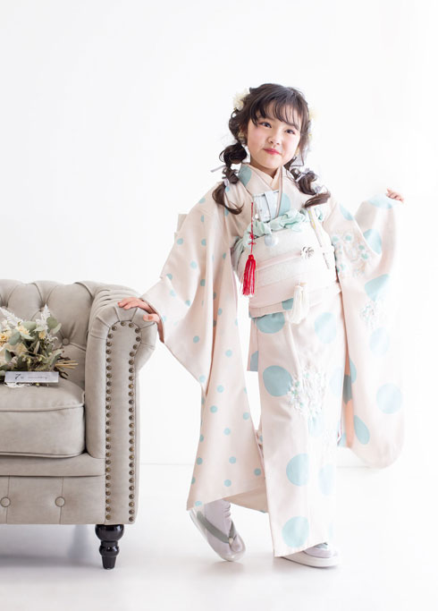 七五三：アイボリーにパステルブルーの大小様々な水玉模様の着物を着て、袖を広げて微笑む7歳の女の子