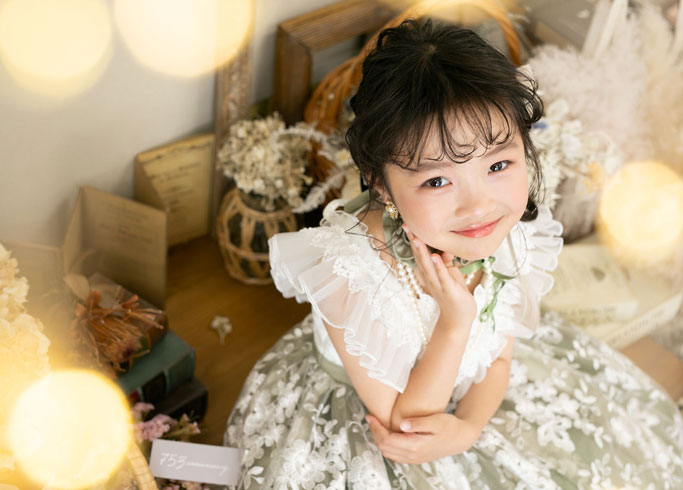 七五三：チュールやフリル飾りが豪華なホワイト×ペールグリーンのドレスを着て、頬に手を当てこちらを見つめる7歳の女の子