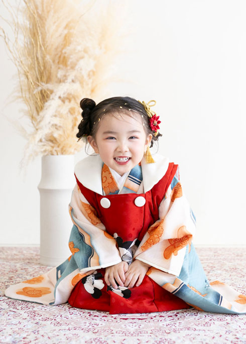七五三：赤い被布と古典柄の着物で、正座をして微笑む3歳の女の子