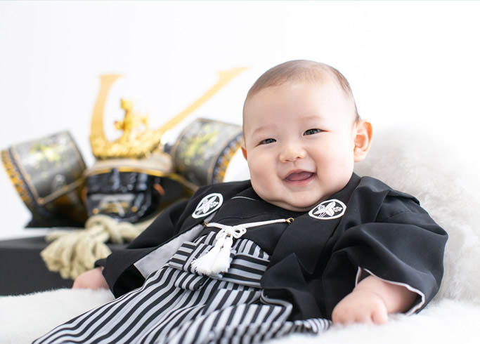 端午の節句：兜飾りと並んで黒紋付きを着た男の子の赤ちゃん。