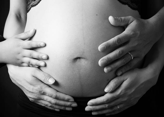 マタニティ：モノクロフォト。パパ、ママ、子どもの三人の手でママの大きなお腹を包み込んだ写真