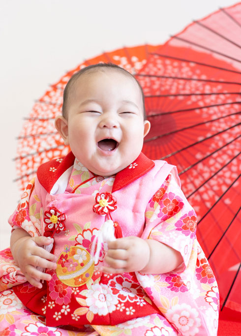 桃の節句：ピンクの着物を着て満面の笑顔の女の子の赤ちゃん。