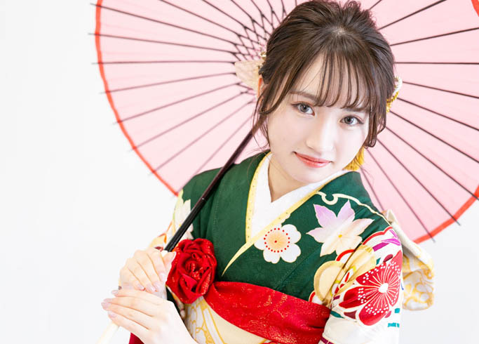 成人：緑色の古典柄振袖を着て赤い和傘を両手で持つ、二十歳の女性