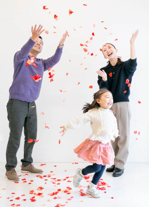 ファミリーフォト：パパママが巻いた花びらの中ではしゃぐ女の子の素敵な家族写真。