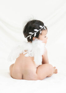 ベビーバースデー：天使の羽と月桂樹の髪飾りを付け一人でお座りをした生後6か月の赤ちゃん