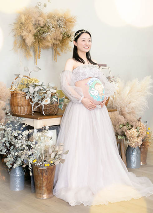 マタニティベリーペイント：くすみピンクのエレガントなマタニティドレスを着たママになる女性。