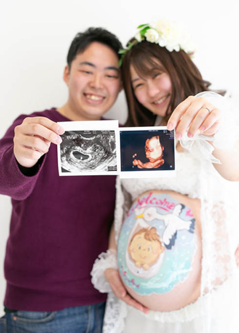 マタニティ：ベリーペイントをしたお腹のママと、エコー写真を持ったパパとの笑顔のツーショット