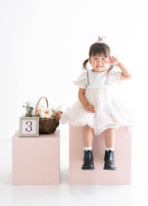 ベビー・バースデー：オシャレなサスペンダースカートにブーツを合わせポーズをとる3才の女の子。