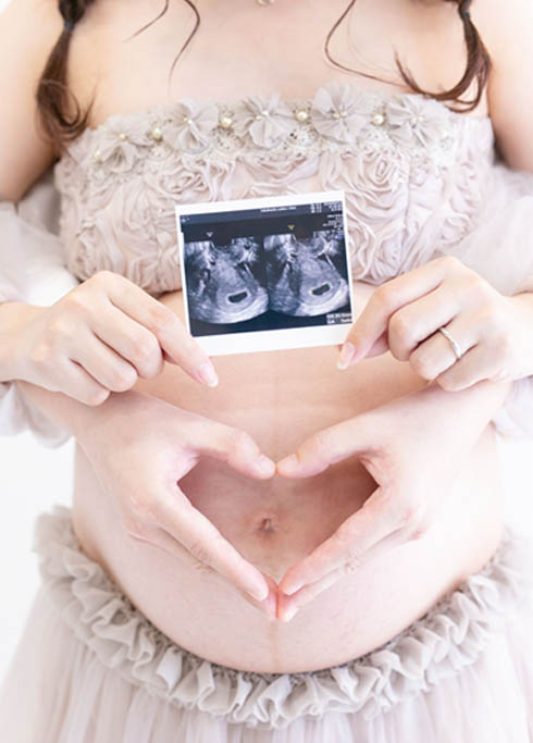 マタニティ：ママのお腹にパパがハートのハンドサイン、ママの手にはエコー写真のアップショット