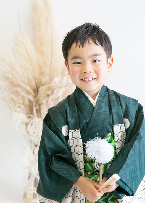 七五三：深い緑の羽織袴に扇子を持ち、やさしく微笑む5歳の男の子
