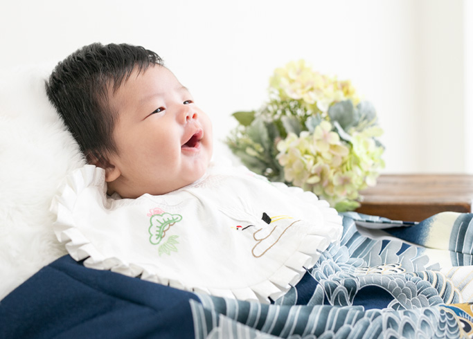 お宮参り：濃紺の古典柄の産着を着て、お口を開けて笑っているように見える男の子の赤ちゃん