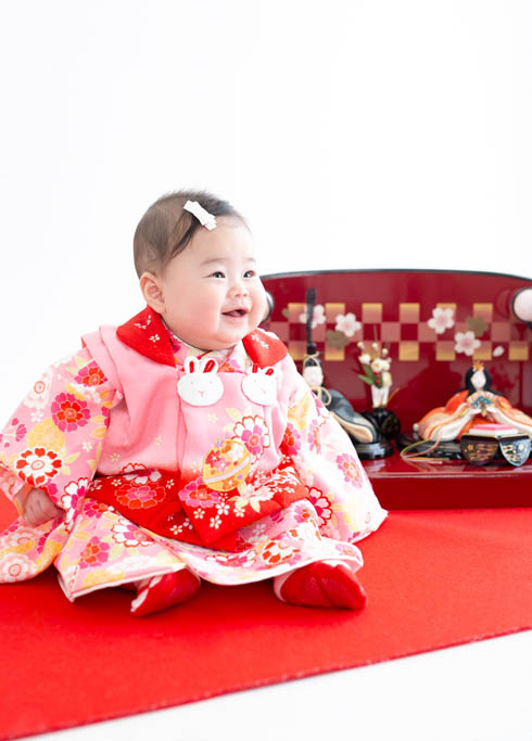 桃の節句：ピンクの着物を着たひな人形と並んだ笑顔の赤ちゃん。