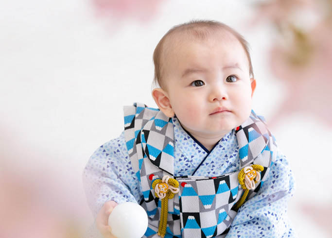 お節句：水色のベビー着物を着て桜の木越しに天を見つめる男の子の赤ちゃん