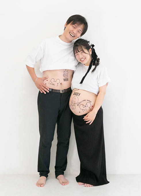 マタニティ：白Tシャツに黒いボトムでペアルックをしたパパとママが仲良くお腹を出したツーショット