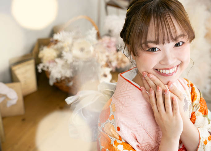 成人：薄ピンク色の振袖を着てネイルの綺麗な手を顔に添えカメラを見つめる20歳の女性