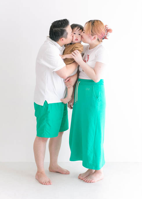 ファミリーフォト：パパとママから両ほっぺにキスを受ける小さな男の子がかわいい家族写真。