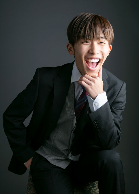 成人：スリーピーススーツを着て椅子に腰かけ、笑顔の成人男性