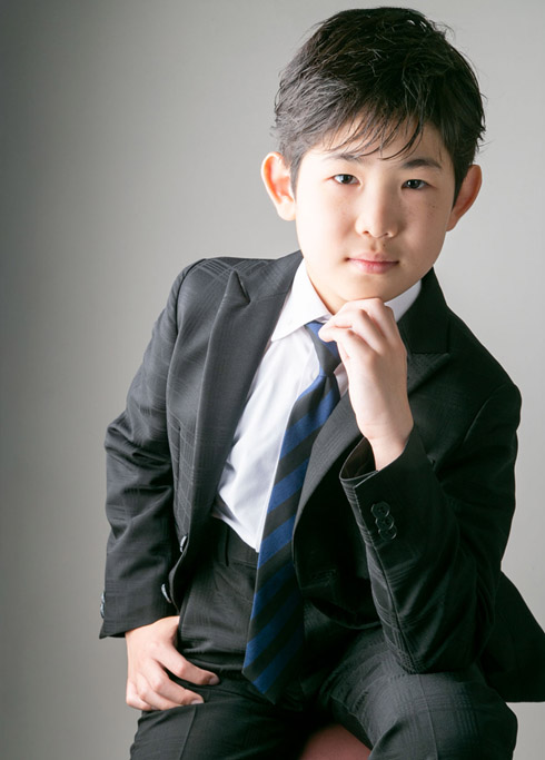 ハーフ成人：黒いスーツを着て椅子に腰かけ、オトナっぽいポーズを決める10歳男の子