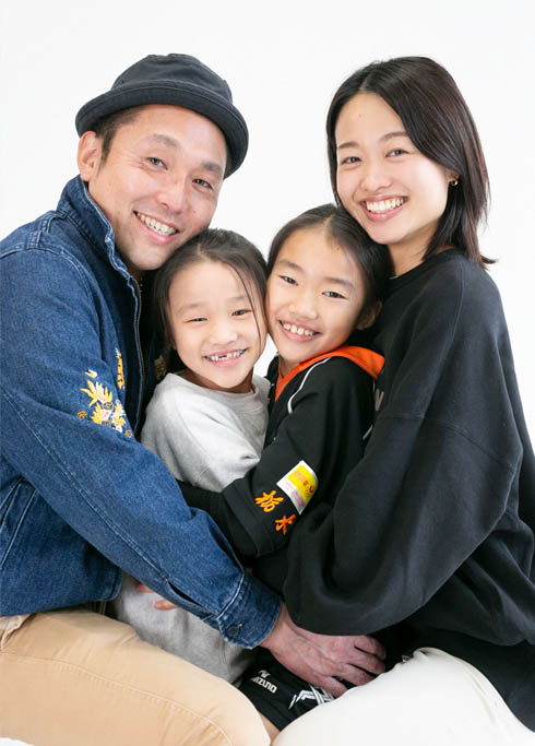 ファミリーフォト：パパママにハグされてうれしそうな姉妹の家族写真。