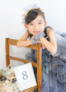 ベビー・バースデー：グレーのフリルの豪華なドレスを着て椅子にもたれる8才の女の子。