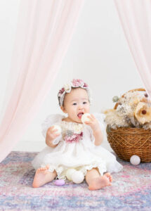 ベビーバースデー：お花や付きの白いベビードレスを着て座っている1歳の女の子