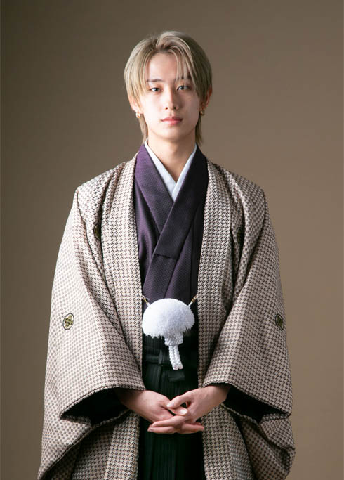 成人：紋付き袴を着て前で手を組みカメラを見つめる、金髪の二十歳の男性