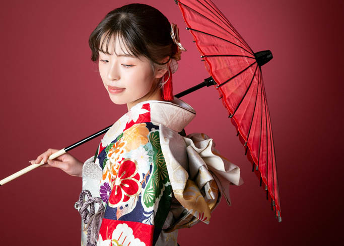 成人：白、赤、青と鮮やかな色柄の振袖を着て赤い和傘をもちポージングをする20歳女性
