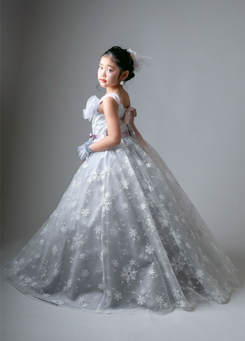 ハーフ成人：雪の結晶の柄のドレスを着てこちらを振り返り見つめる10歳女の子