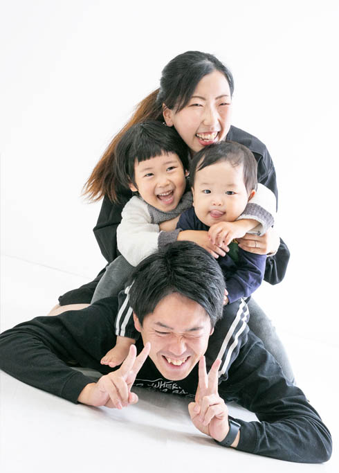 ファミリーフォト：パパの上に重なる二人の小さな男の子とママがかわいい笑える家族写真。