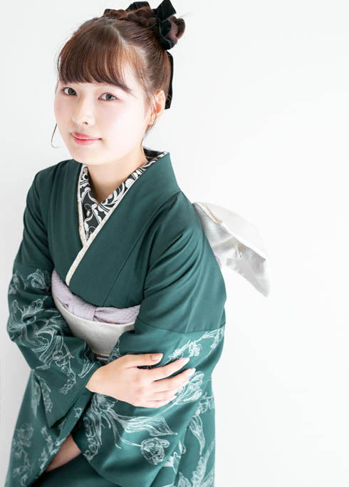 成人：緑色で袖にはボタニカルな花柄の振袖を着てポージングをする茶髪の成人女性