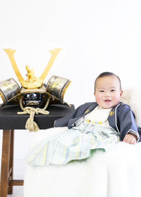 端午の節句：兜飾りと並びにっこり笑う男の子の赤ちゃん。