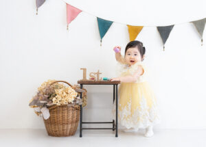 ベビー・バースデー：黄色いドレスを着てつかまり立ちをする1才の女の子。