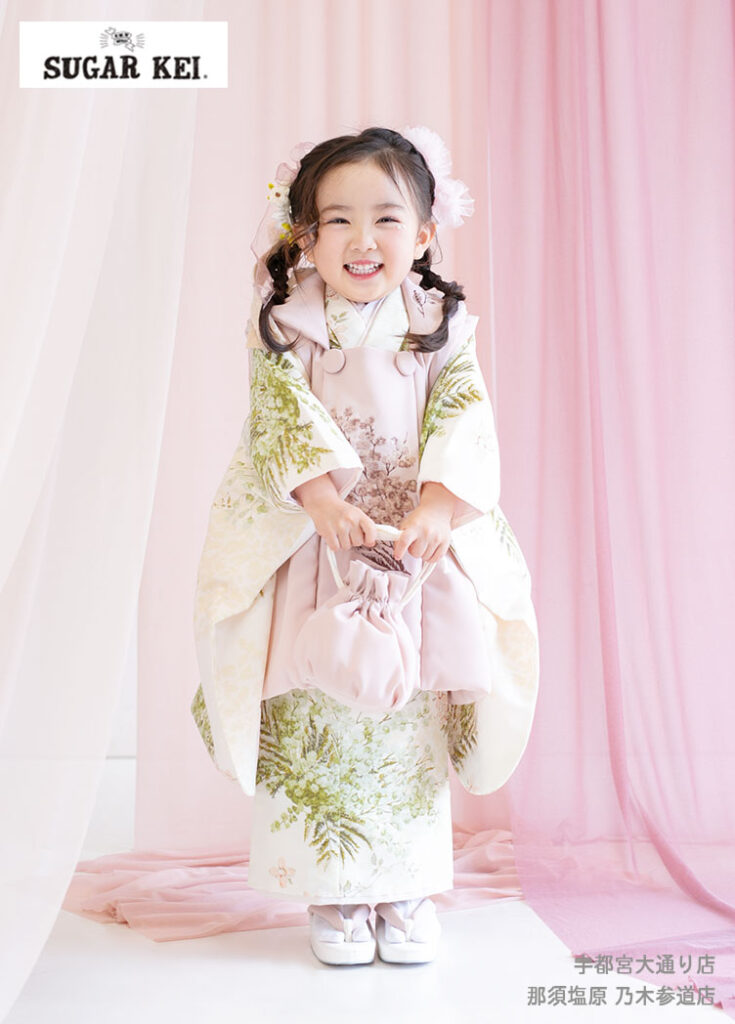 七五三３歳：かわいらしいピンクお被布におしゃれなミモザ柄の着物を着た３才の女の子。