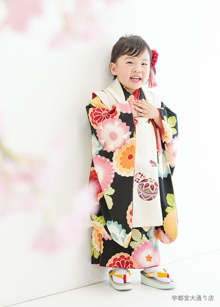 七五三３歳：黒のポップな花柄に白い被布を合わせた着物を着た3才の女の子。