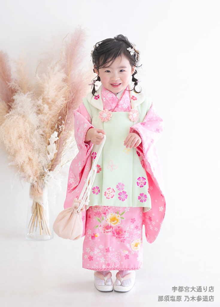 七五三３歳：かわいいピンクの花模様に薄いグリーンの被布の着物を着た3才の女の子。
