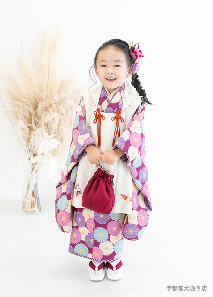 七五三３歳：クラシカルな花柄を一面にあしらった赤紫色の着物を着た3才の女の子。