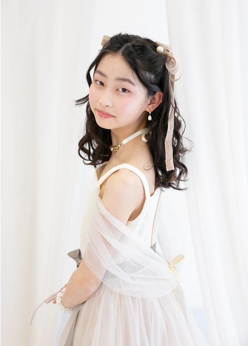 ハーフ成人：淡いベージュのドレスを着て髪にリボンを付けた10才の女の子。